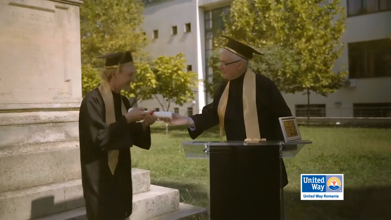 Diplomas handed out at a podium on a sunny campus.